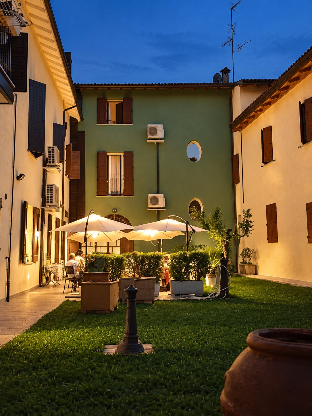 Corte interna del ristorante con prato, ombrelloni e tavoli all'imbrunire